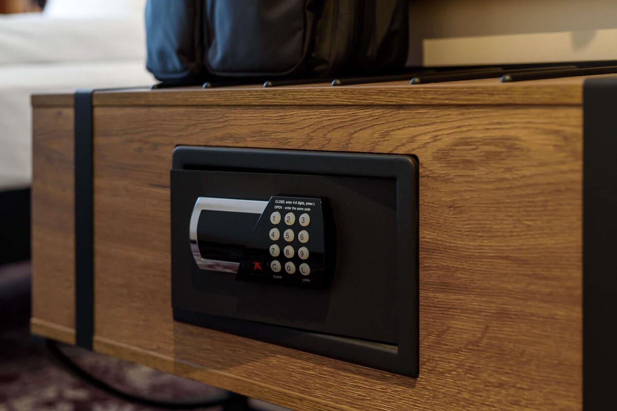 Habitación de hotel con un cajón de madera que contiene un dispositivo electrónico negro, posiblemente una caja fuerte o sistema de bloqueo.