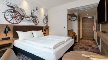 Ett hotellrum med en säng, sängbord, ett skrivbord, en stol, ett runt bord med en flaska på, en klädställning, en garderob och en tv.