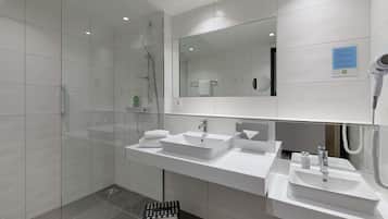 A modern bathroom with a glass shower enclosure, two sinks, a hairdryer, and a towel rack.