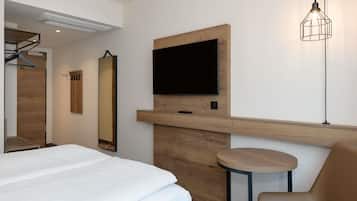 A modern hotel room with a bed, a mounted TV, a wooden accent wall, a mirror, and a small round table with a chair.