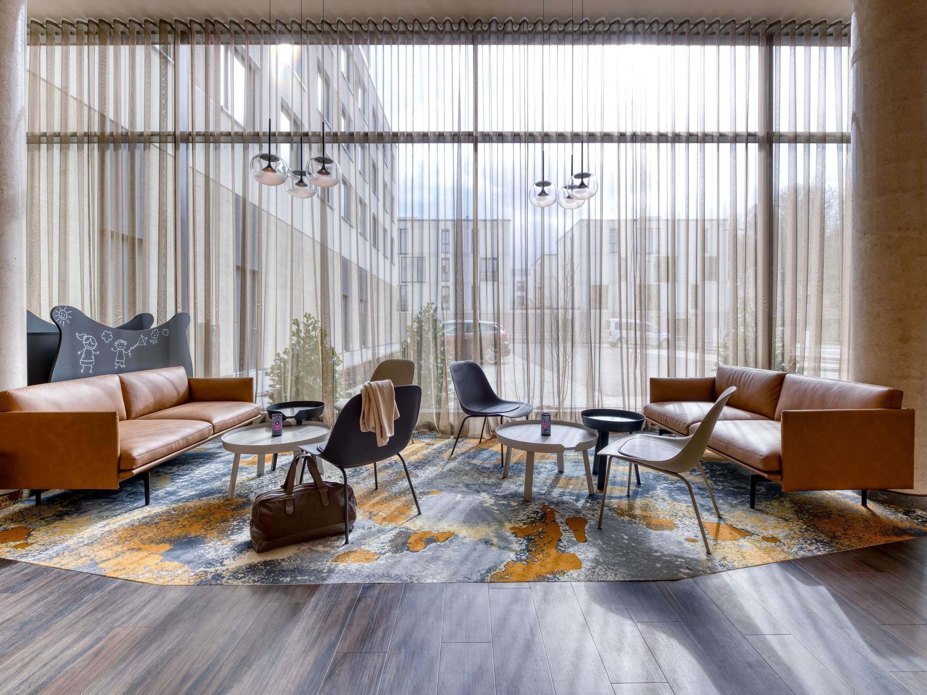 Un salon moderne avec des canapés en cuir, un tapis à motifs et une grande fenêtre ornée de rideaux légers.