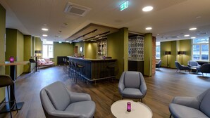 A modern lounge area with bar seating, a round table, and a decorative partition. - Ibis Styles Coburg (Coburg)