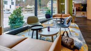 A modern hotel lobby with large windows, seating areas, and a view of the street. - Ibis Styles Coburg (Coburg)