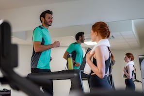 Un gimnasio con cintas de correr, una botella de agua y un espejo que refleja el espacio.