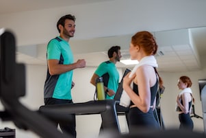 Un gimnasio con cintas de correr, una botella de agua y un espejo que refleja el espacio.