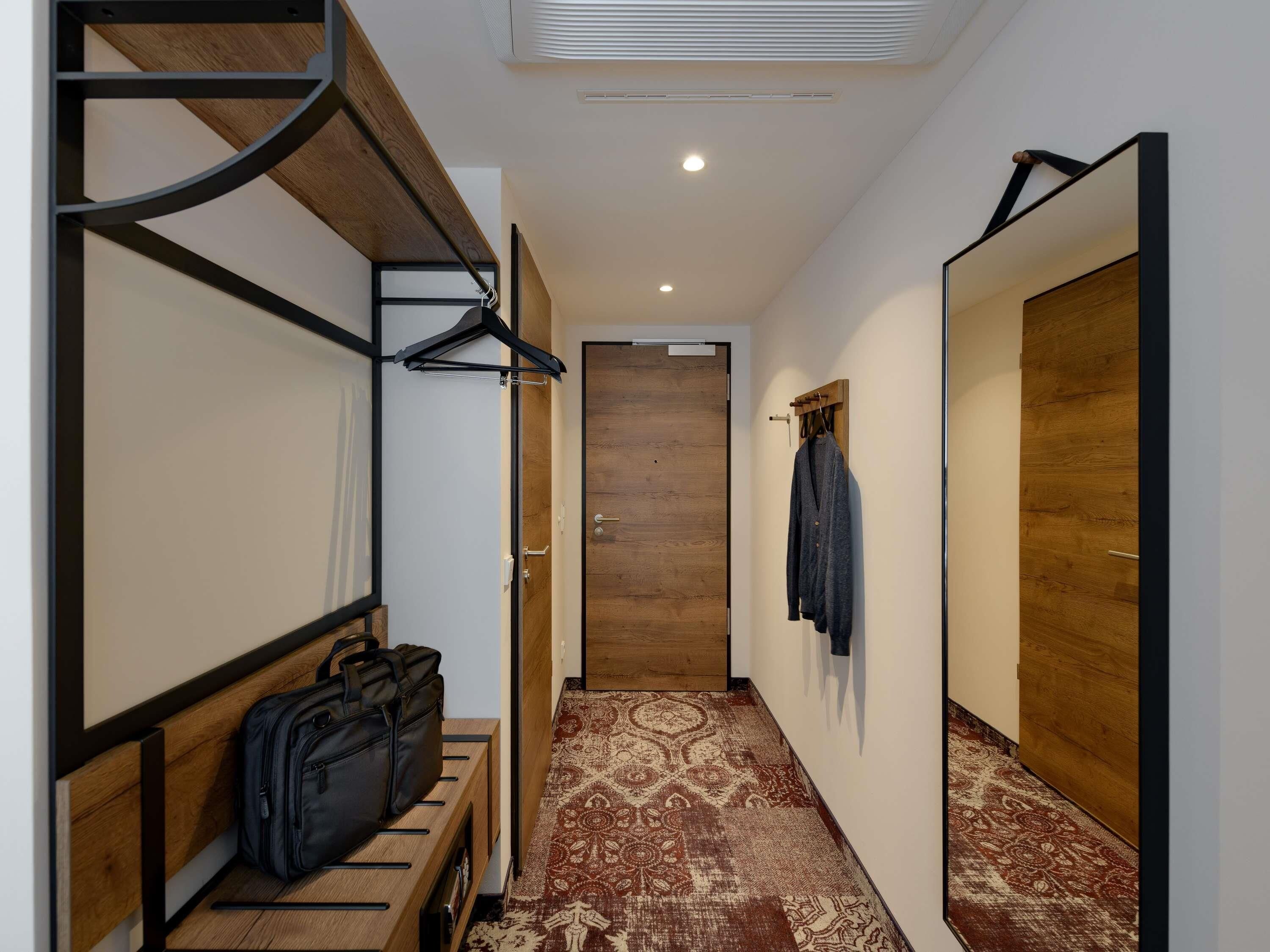 Un couloir avec un banc, un porte-manteau suspendu, une porte en bois et un tapis à motifs.