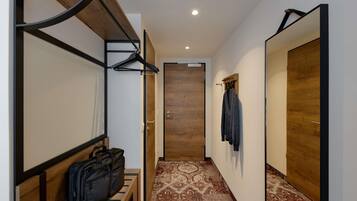 Un couloir avec un banc, un porte-manteau suspendu, une porte en bois et un tapis à motifs.
