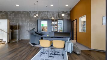 Modernilla designilla varustettu hotellin vastaanottoalue, johon kuuluu vastaanottotiski, oleskelualue ja seinälle asennettu näyttö, jossa esitetään tietoa.