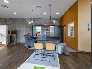 A hotel reception area with a modern design, including a reception desk, seating area, and a wall-mounted screen displaying information. - Ibis Styles Coburg (Coburg)