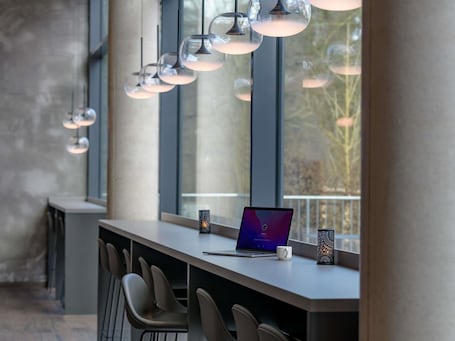 Un área de bar moderna con una laptop, una taza y un accesorio de luz decorativo.. Ibis Styles Coburg