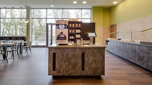 A modern cafe with a marble counter, a coffee machine, and a display of pastries. - Ibis Styles Coburg (Coburg)