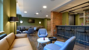 A modern lounge area with a sofa, armchairs, a small table, and a bar with stools. - Ibis Styles Coburg (Coburg)