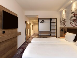Habitación de hotel con una cama grande, un televisor de pantalla plana en la pared, cabecera de madera, armario con espejo y estante con una bicicleta y una rueda roja.