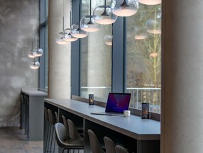 A modern bar area with a laptop, a mug, and a decorative light fixture. - Ibis Styles Coburg (Coburg)