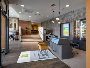 A modern reception area with a digital display, seating, a staircase, and a vending machine.