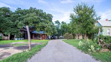 Een grindpad leidt naar een landelijk huis met een blauw dak, omgeven door weelderige begroeiing en bomen.