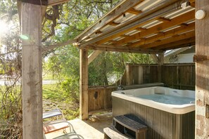 A wooden outdoor hot tub area with a pergola overhead, surrounded by trees and a wooden fence.