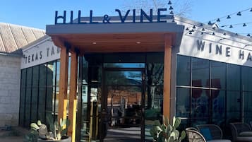 El exterior de Hill & Vine Wine House, con entrada despejada, zona de estar al aire libre y un letrero que indica que es un lugar para ir, comer y divertirse.