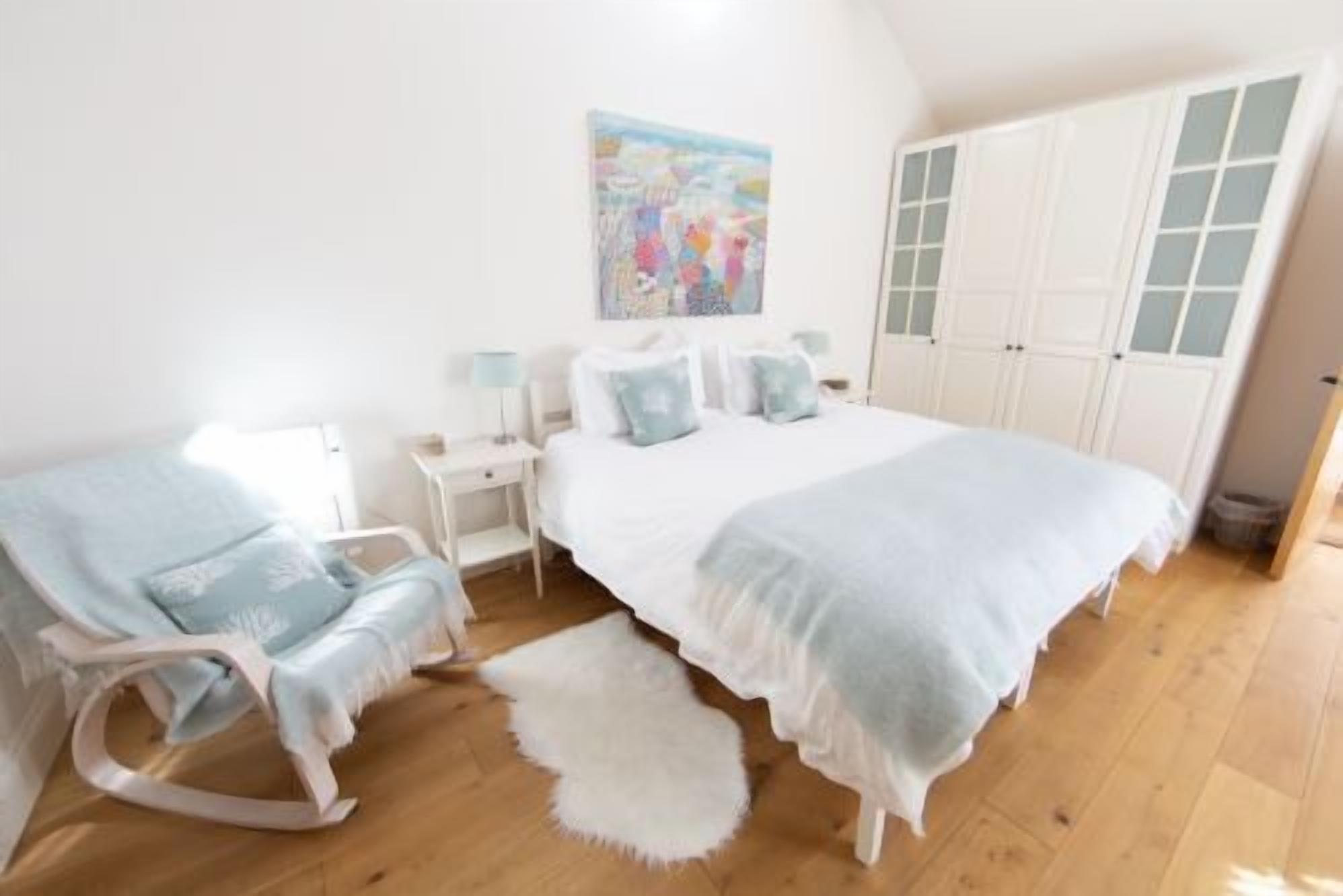 A bedroom with a bed, a chair, a nightstand, a lamp, and a painting on the wall.