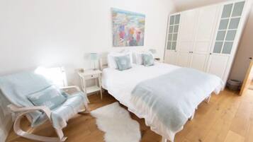 A bedroom with a bed, a chair, a nightstand, a lamp, and a painting on the wall.