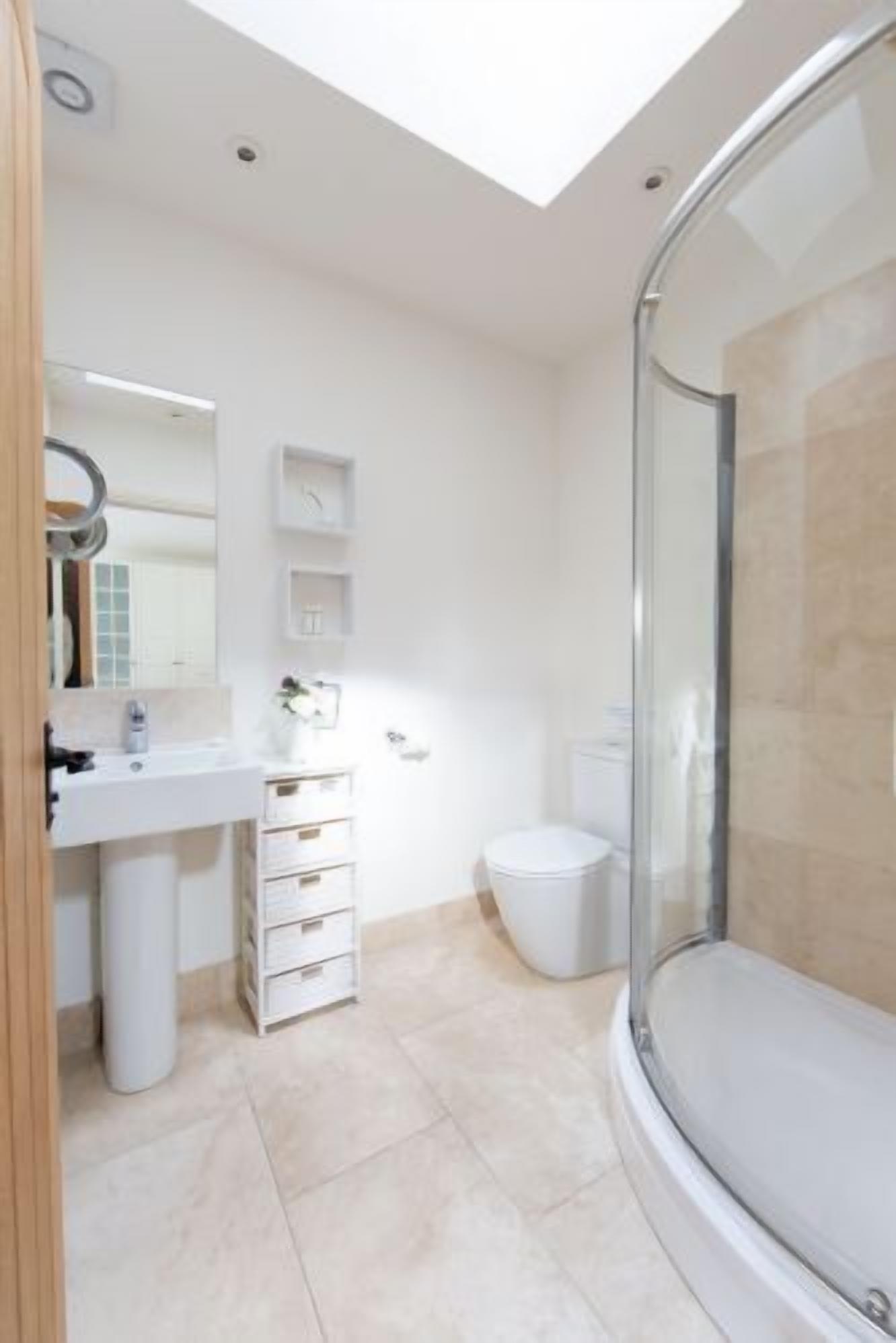 Ein modernes Badezimmer mit Duschkabine aus Glas, einem weißen Waschbecken und einer Toilette.