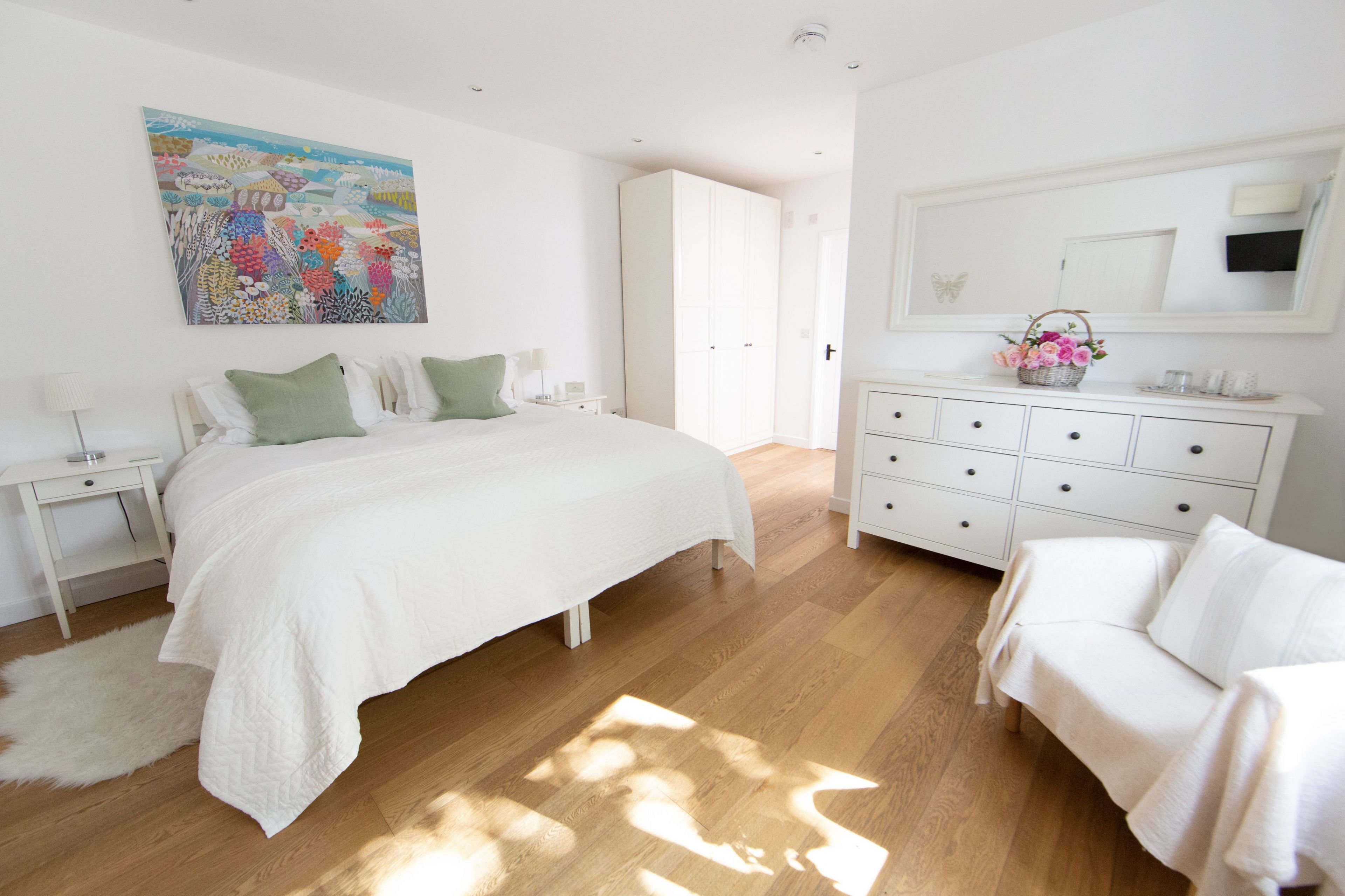 A bedroom with a large bed, a white dresser, a white sofa, and a painting on the wall.