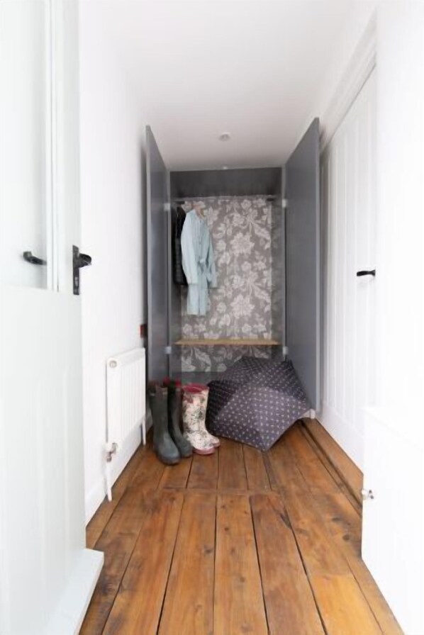 A narrow hallway with wooden flooring, a radiator, a hanging coat rack, and a patterned curtain.