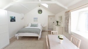 Un dormitorio con cama, una mesita de noche con un florero y una ventana con cortinas.