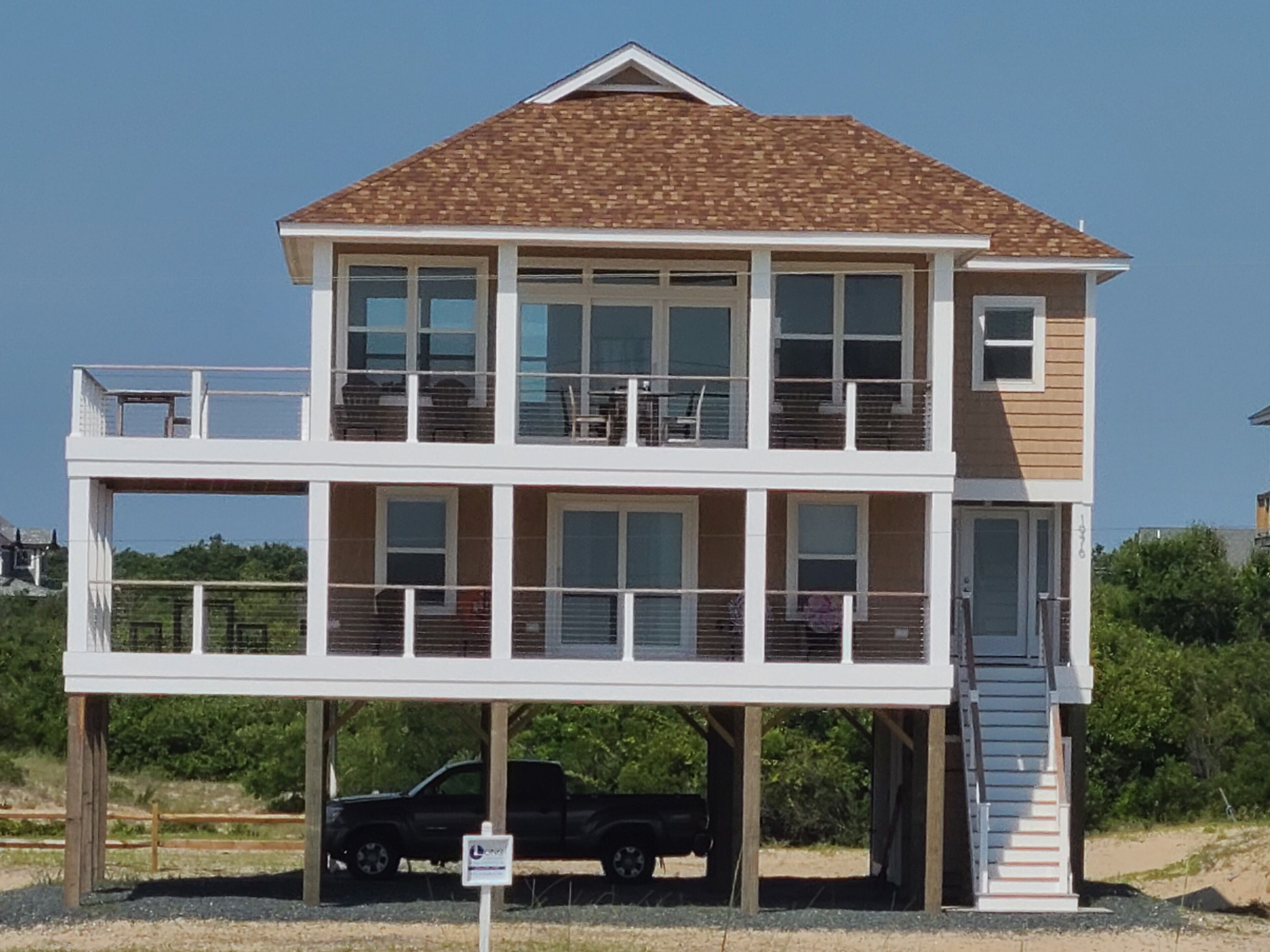 Una casa fronte spiaggia su due piani, con un balcone al piano superiore e un garage al piano terra.