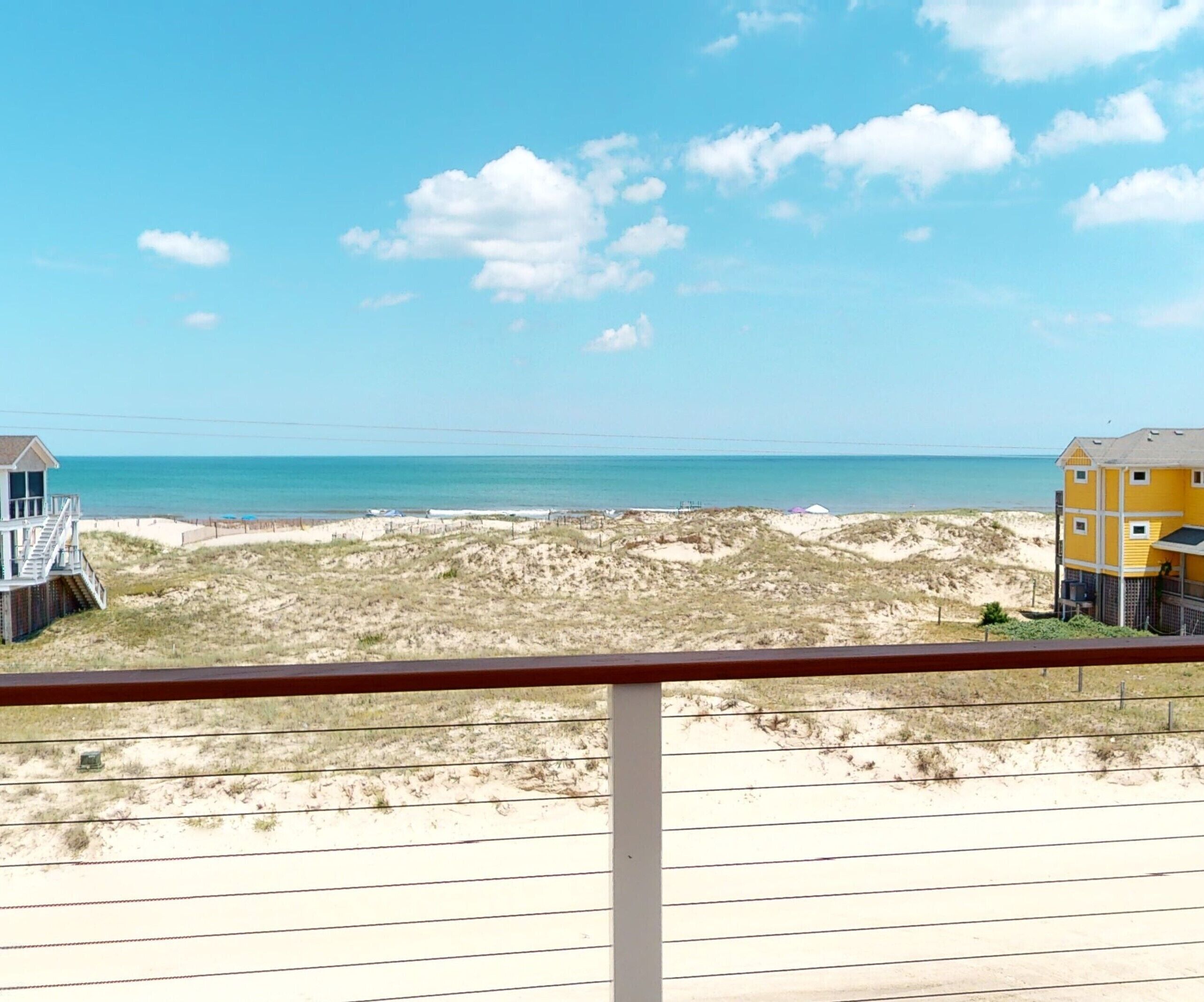 A beach view with a wooden deck and a yellow building in the background.