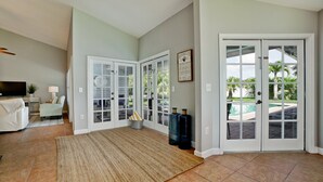 Ampla sala de estar com uma TV grande, assentos confortáveis e vista para uma piscina através de portas de vidro.