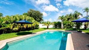 Piscina com dois guarda-sóis, cercada por vegetação exuberante e palmeiras.