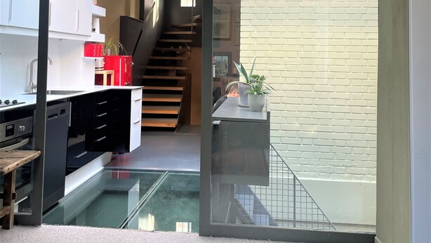 Una cocina moderna con un separador de vidrio, una escalera que sube a un altillo y una pared de ladrillo.