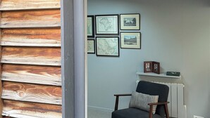 Una habitación con pared exterior de madera, una silla, un tapete y cuadros en la pared.