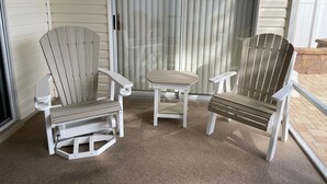 A covered porch with two Adirondack chairs and a small table.