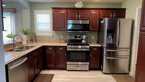 A modern kitchen with wooden cabinets, stainless steel appliances, and a large window with blinds.