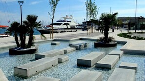 Un port de plaisance où sont amarrés des yachts, une piscine avec des marches en béton et des palmiers.