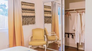 A bedroom with a bed, a yellow armchair, a wardrobe, and two wall hangings.