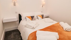 Een hotelkamer met een bed, twee wandlampen, een witte nachtkastje en een donker vloerkleed.