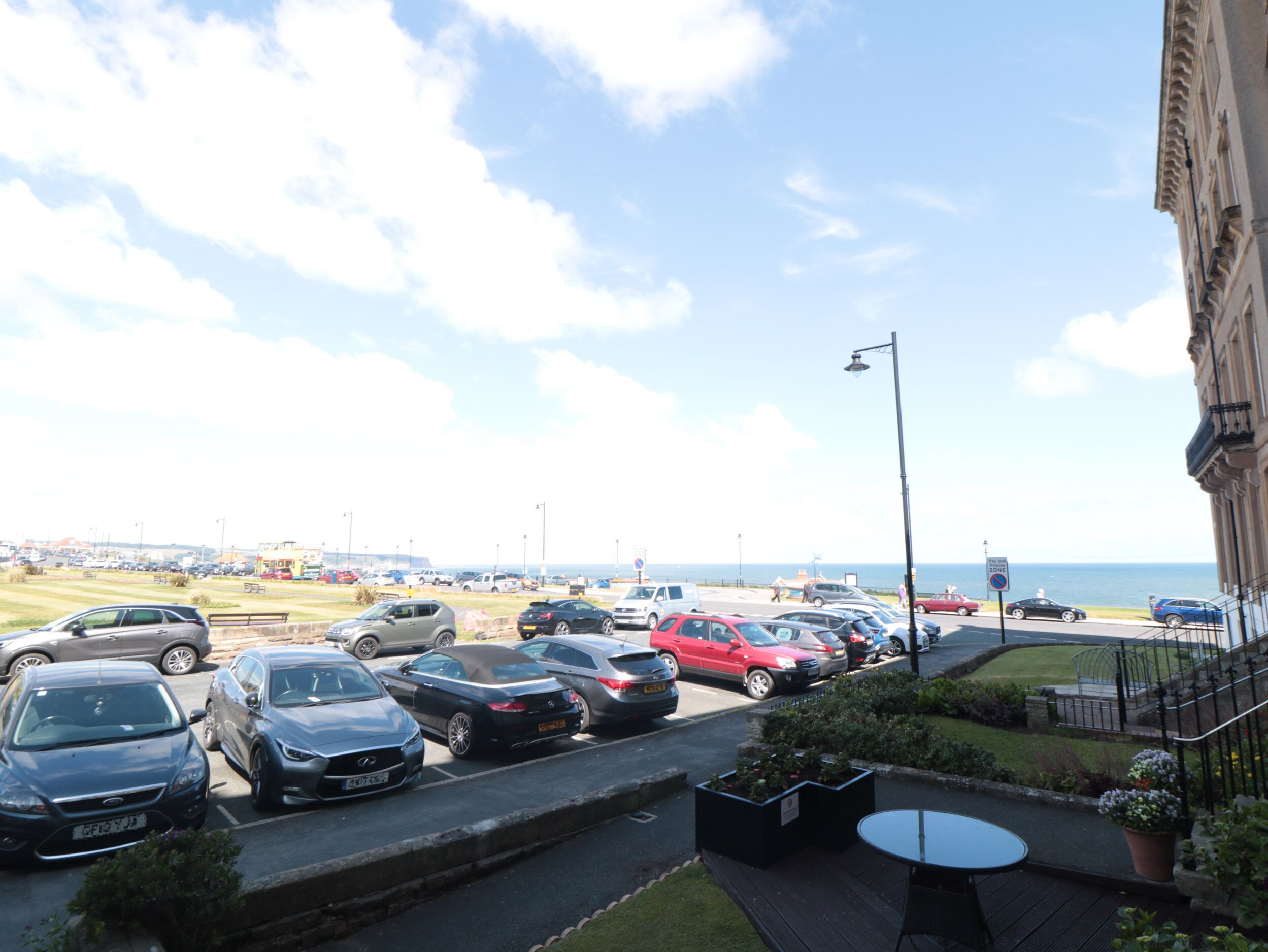 A parking area with various cars, a street lamp, and a view of the sea.
