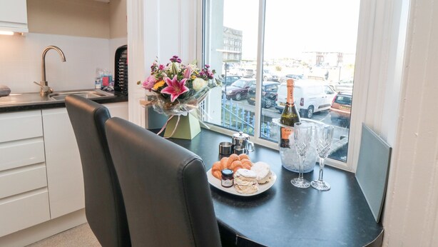 Een moderne keuken met een eettafel gedekt voor twee personen, een bloemenboeket, een fles champagne en een bord scones.