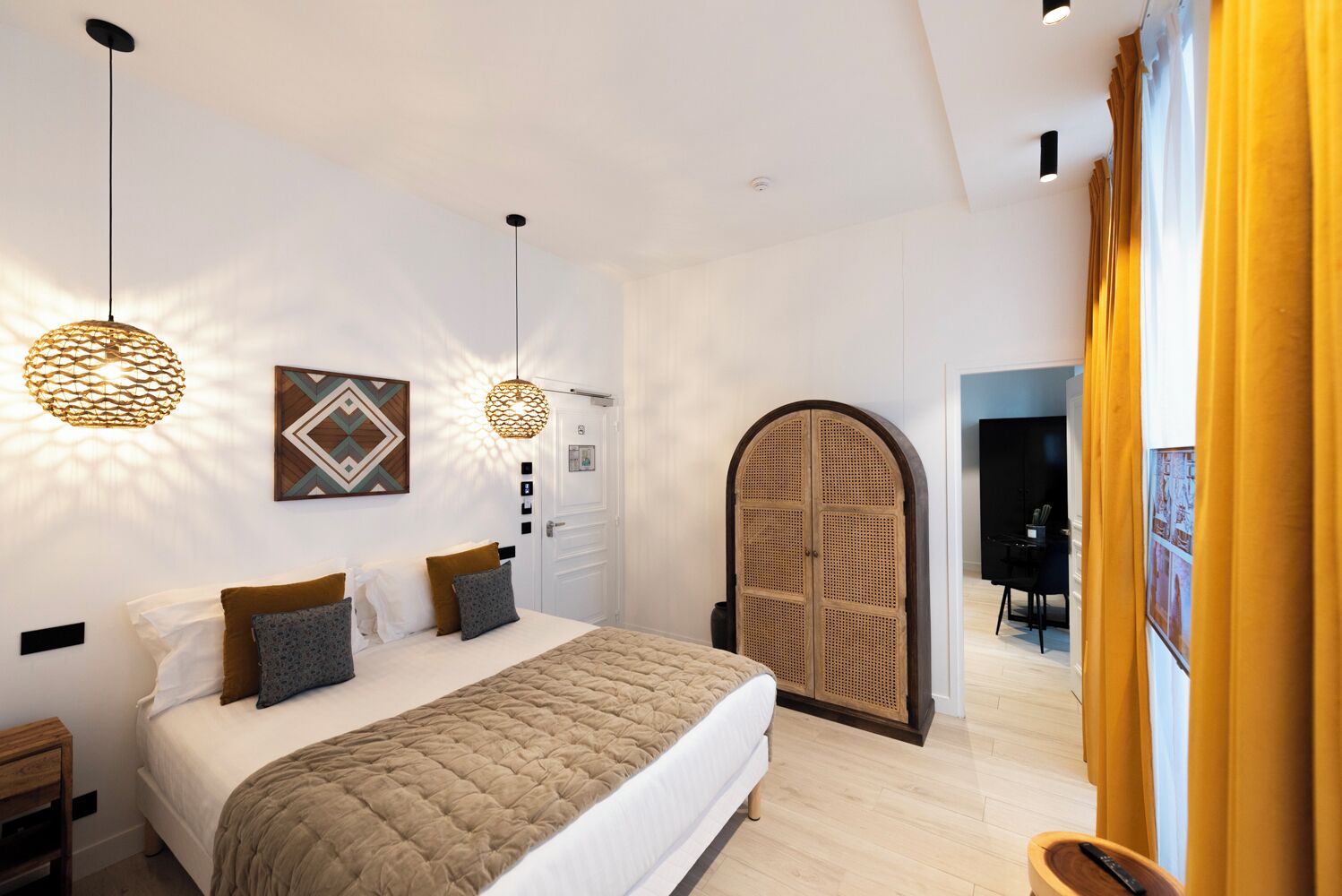 A modern bedroom with a large bed, two pendant lights, a decorative wall piece, and a rattan wardrobe.