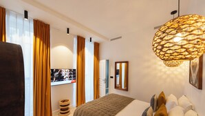 Ein modernes Hotelzimmer mit einem großen Bett, einem Fernseher, einer besonderen Hängeleuchte und Blick ins Freie.
