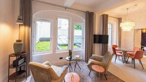 A modern living room with large windows, a flat-screen TV, and a dining area with orange chairs. - Lovelace, 4 stars Residence, Luxury at 50 meters from the Champs-Elysées (París)