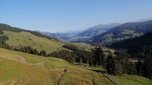 A panoramic view of a mountainous landscape with a winding road, green fields, and scattered buildings. - Urlaub in den Bergen (Uderns)