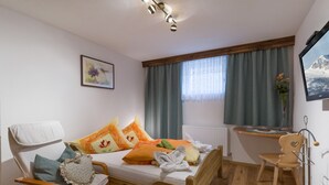 A cozy bedroom with a wooden bed, a chair, a desk, and a window with curtains. - Urlaub in den Bergen (Uderns)