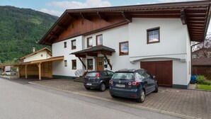 A two-story building with a wooden facade, a garage, and two parked cars. - Urlaub in den Bergen (Uderns)
