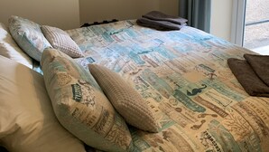 Una cama bien hecha con ropa de cama estampada, un perchero con ropa y una pequeña bolsa blanca que dice "hairy".