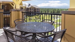 A covered outdoor area with a round table and chairs, a view of a building and forest in the background.