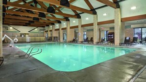 An indoor swimming pool with a clear water surface, surrounded by lounge chairs and a tiled floor.